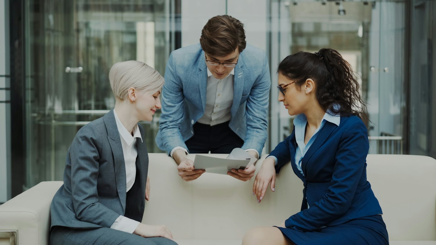 Ein diverses Business-Team bespricht Dokumente auf einem modernen Bürosofa.